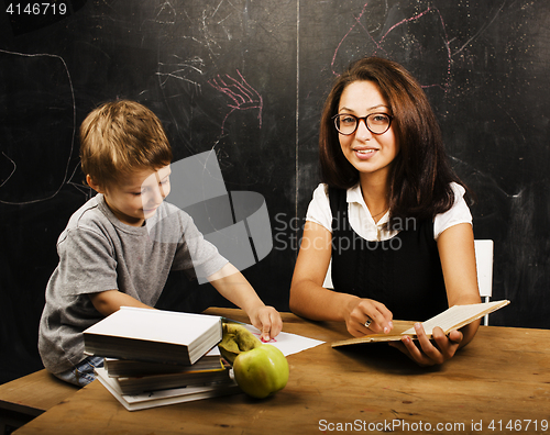 Image of little cute boy with young teacher in classroom studying at blac