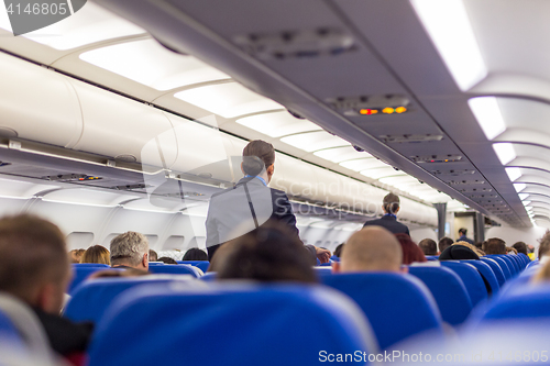 Image of Stewardess walking the aisle of commercial airplane.