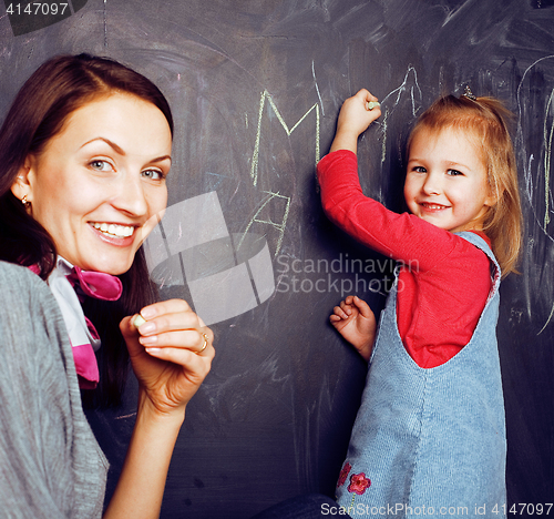 Image of cute cheerful teacher with little pupil in classroom at blackboard learning, happy smiling, lfestyle people concept