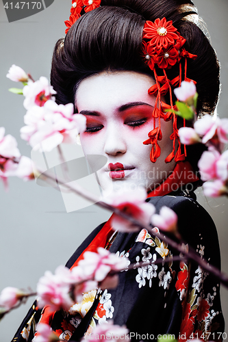 Image of young pretty geisha in black kimono among sakura, asian ethno