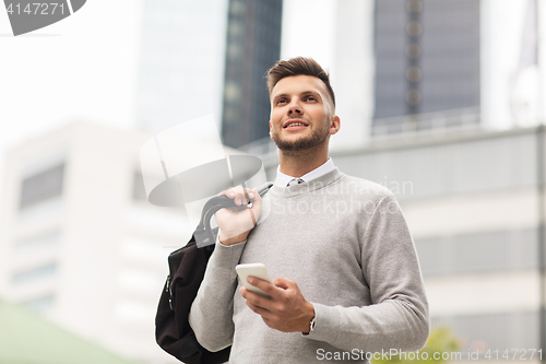 Image of happy young man with smartphone and bag in city