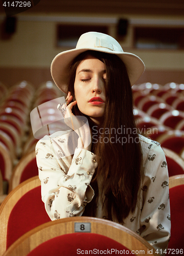 Image of portrait of a pretty girl hipster in a movie theater wearing hat, dreaming alone