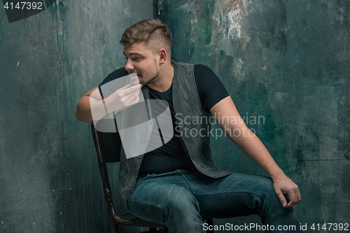Image of Portrait of smiling happy man sitting on the chair in studio