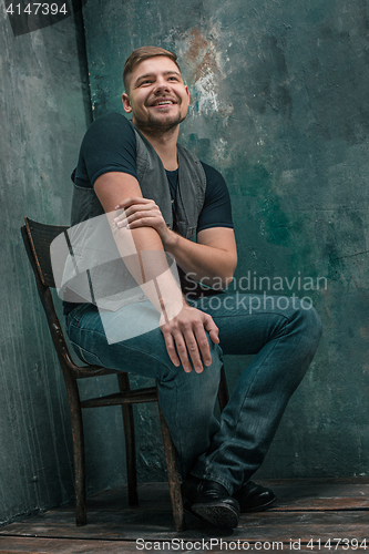 Image of Portrait of smiling happy man sitting on the chair in studio
