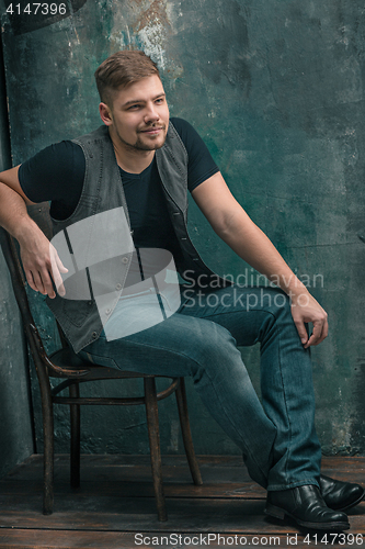 Image of Portrait of smiling happy man sitting on the chair in studio