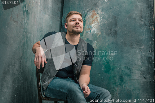 Image of Portrait of smiling happy man sitting on the chair in studio