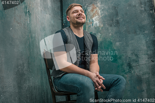 Image of Portrait of smiling happy man sitting on the chair in studio