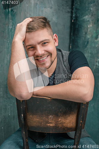 Image of Portrait of smiling happy man sitting on the chair in studio
