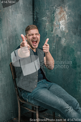 Image of Portrait of smiling happy man sitting on the chair in studio