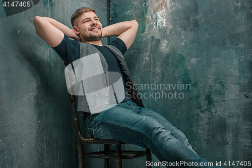 Image of Portrait of smiling happy man sitting on the chair in studio