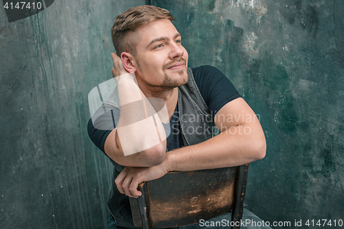 Image of Portrait of smiling happy man sitting on the chair in studio