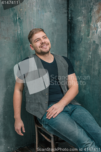 Image of Portrait of smiling happy man sitting on the chair in studio
