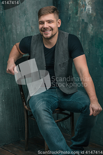 Image of Portrait of smiling happy man sitting on the chair in studio