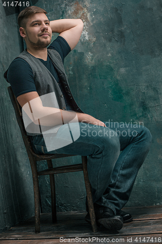 Image of Portrait of smiling happy man sitting on the chair in studio
