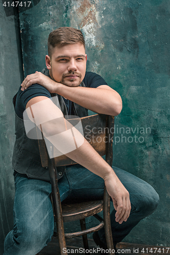 Image of Portrait of smiling happy man sitting on the chair in studio