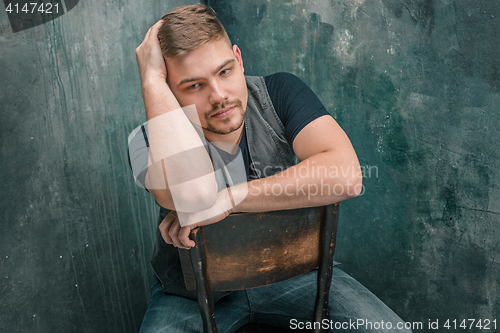 Image of Portrait of serious man sitting on the chair in studio