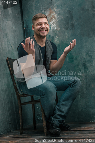 Image of Portrait of smiling happy man sitting on the chair in studio