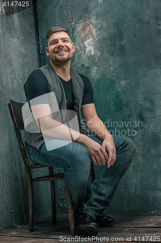 Image of Portrait of smiling happy man sitting on the chair in studio