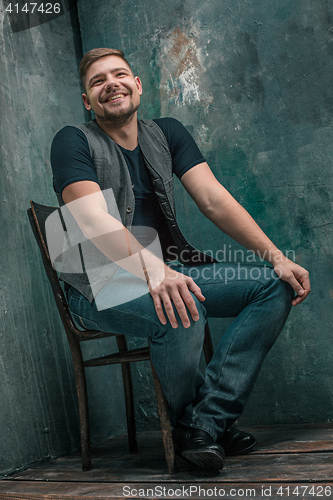 Image of Portrait of smiling happy man sitting on the chair in studio