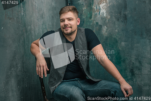 Image of Portrait of smiling happy man sitting on the chair in studio