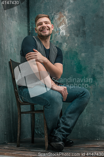 Image of Portrait of smiling happy man sitting on the chair in studio