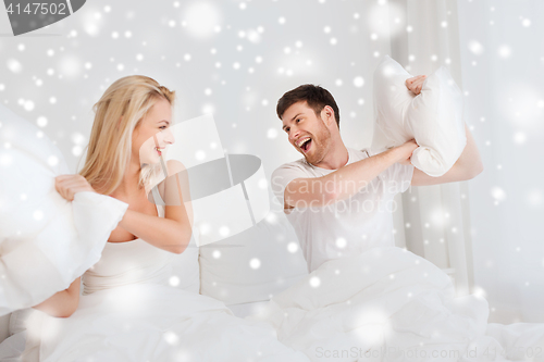 Image of happy couple having pillow fight in bed at home