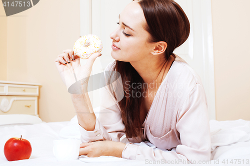 Image of young pretty brunette woman laying in bed, luxury white interior