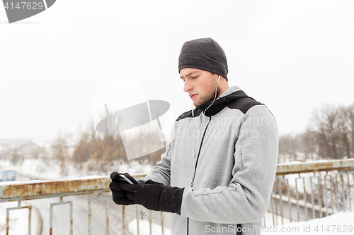 Image of man in earphones with smartphone on winter bridge