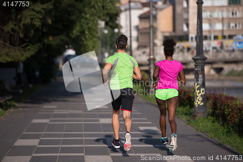 Image of young smiling multiethnic couple jogging in the city
