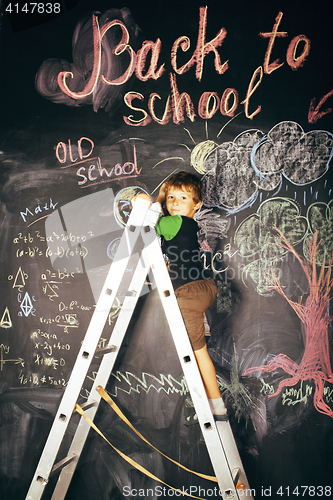 Image of little cute real boy at blackboard in classroom, back to school,