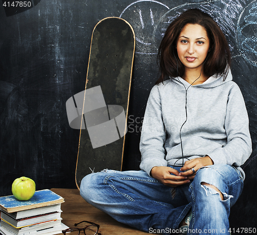 Image of young cute teenage girl in classroom at blackboard seating on ta