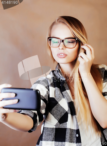 Image of young pretty blond hipster girl making selfie on warm brown back