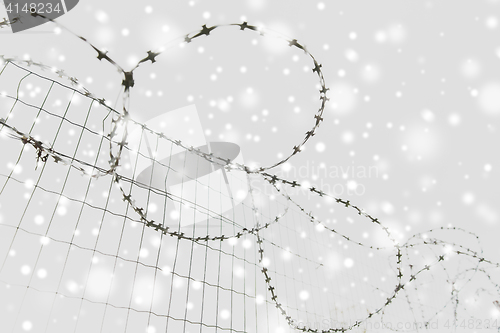 Image of barb wire fence over gray sky and snow