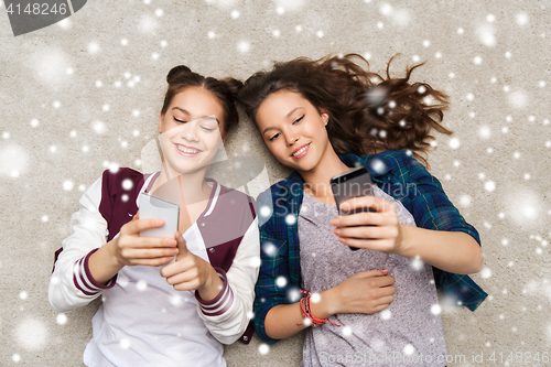 Image of happy teenage girls lying on floor with smartphone