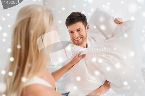 Image of happy couple having pillow fight in bed at home