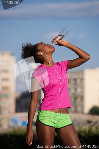 Image of african american woman drinking water after jogging