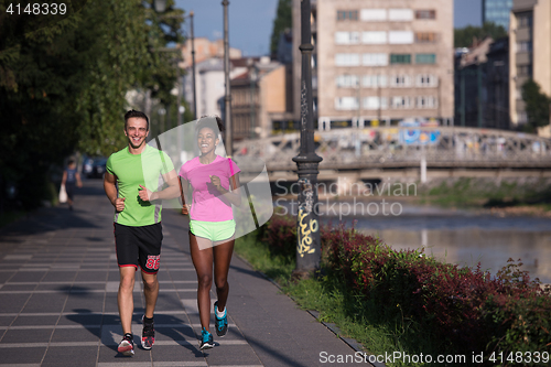 Image of young smiling multiethnic couple jogging in the city