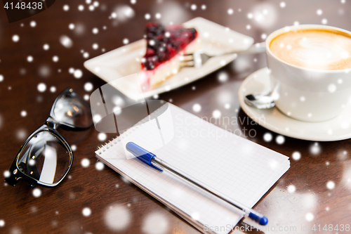 Image of close up of notebook with pen, coffee cup and cake