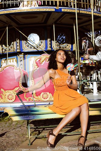 Image of cool real african american teenage girl with candy near carousels at amusement park, lifestyle people concept