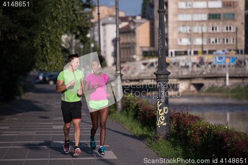 Image of young smiling multiethnic couple jogging in the city