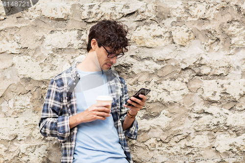 Image of man with smartphone drinking coffee on city street