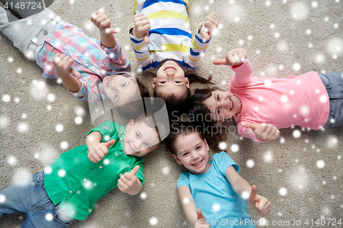 Image of happy kids lying on floor and showing thumbs up