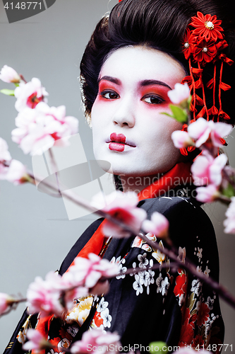 Image of young pretty geisha in black kimono among sakura, asian ethno