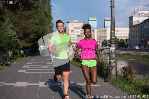 Image of young smiling multiethnic couple jogging in the city