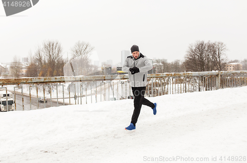 Image of man with earphones running along winter bridge