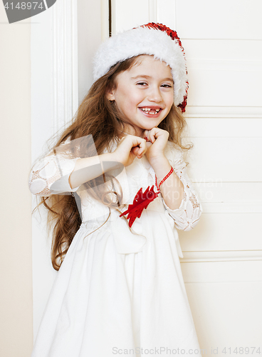 Image of little cute girl in santas red hat waiting for Christmas gifts. smiling adorable kid. White new dress home interior