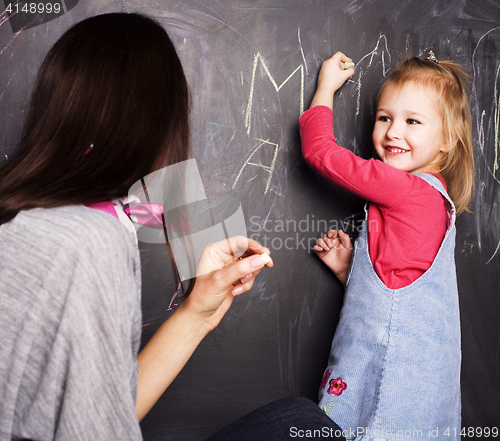 Image of little cute blond girl writing on blackboard in classroom with teacher, lifestyle education people concept