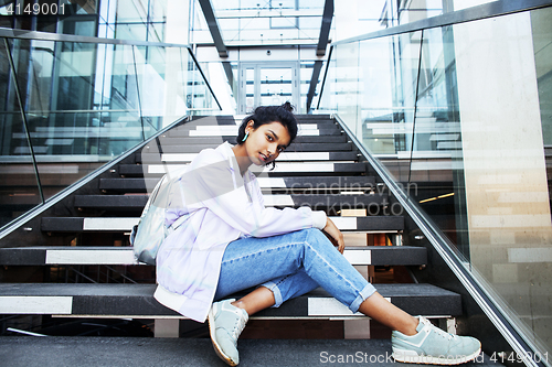 Image of young cute modern indian girl at university building sitting on stairs reading a book, wearing hipster glasses, lifestyle people concept