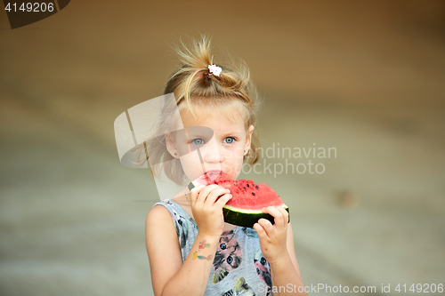 Image of Adorable blonde girl eats a slice of watermelon outdoors.