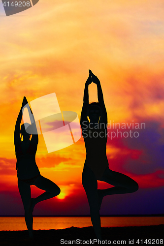 Image of Yoga people training and meditating in warrior pose outside by beach at sunrise or sunset.